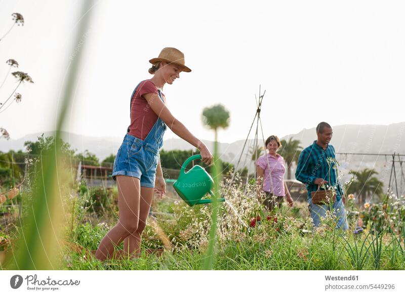 Smiling young farmer with watering can and friends in the background garden gardens domestic garden woman females women gardener gardeners Adults grown-ups