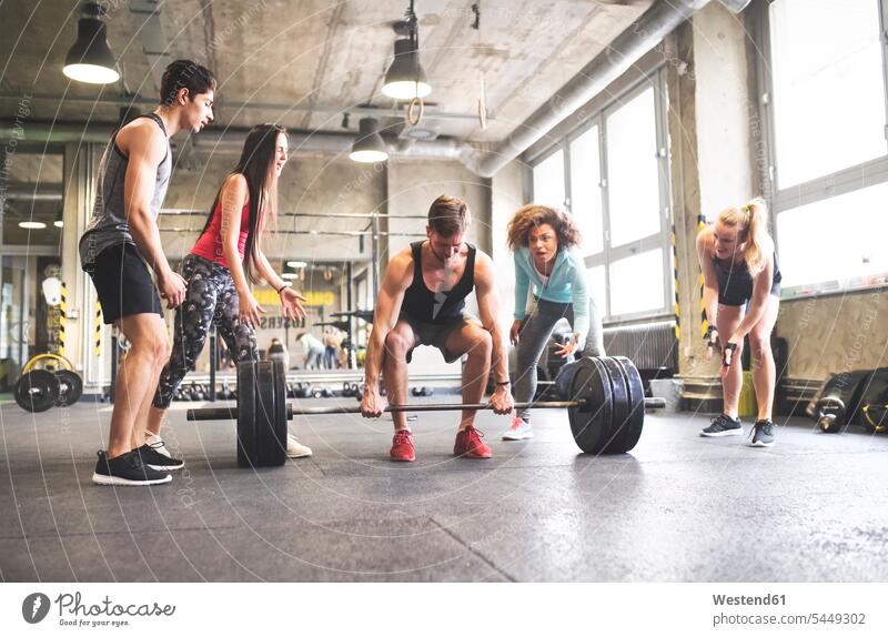 Group of young fit people cheering at man weightlifting in gym weight lifting exercising exercise training practising strength sports gyms Health Club fitness