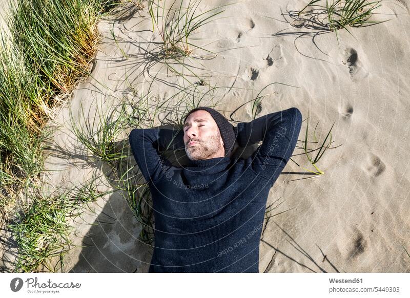 Man wearing woolly hat lying in beach dune sand dune sand dunes beaches sleeping asleep relaxed relaxation laying down lie lying down man men males relaxing