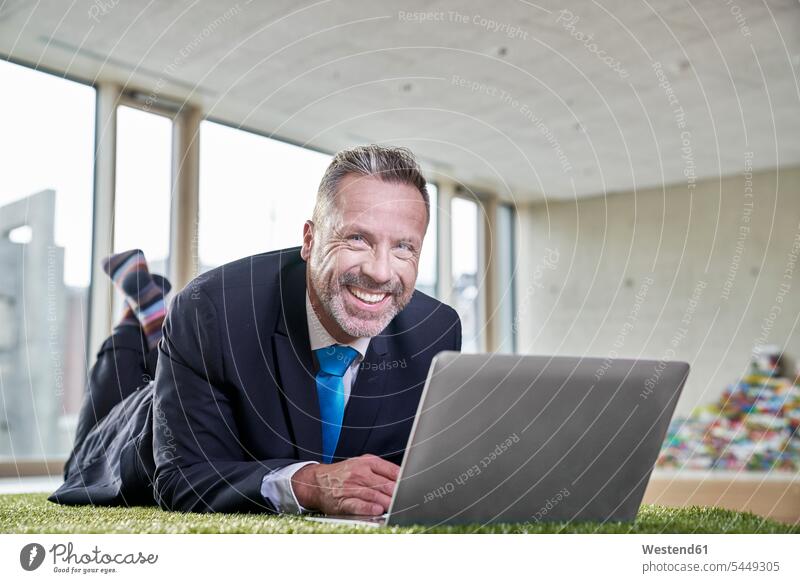 Happy businesssman lying on synthetic turf using laptop Businessman Business man Businessmen Business men Laptop Computers laptops notebook smiling smile