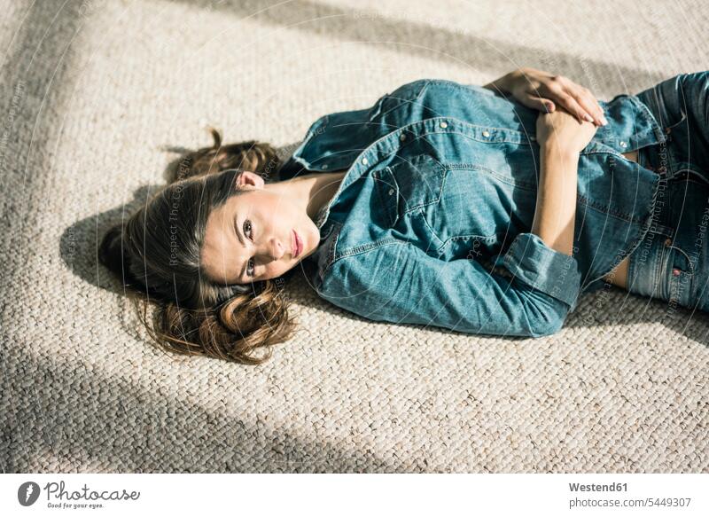 Portrait of oung woman lying on carpet in the living room enjoying sunlight laying down lie lying down portrait portraits females women Adults grown-ups