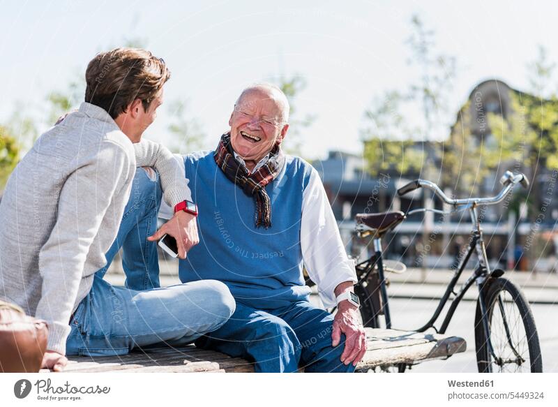 Laughing senior man with adult grandson on a bench happiness happy grandfather grandpas granddads grandfathers benches grandsons laughing Laughter sitting