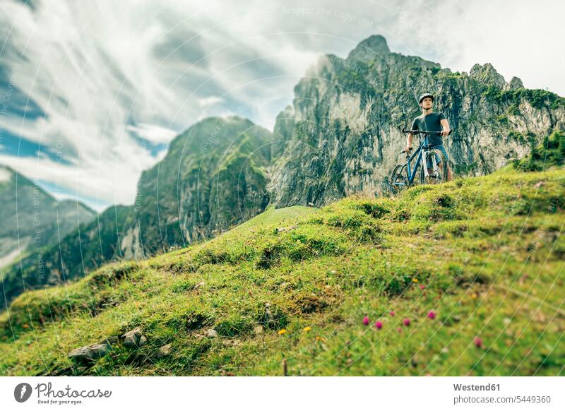Germany, Bavaria, Pfronten, young man with mountain bike on alpine meadow near Aggenstein View Vista Look-Out outlook men males standing Adults grown-ups