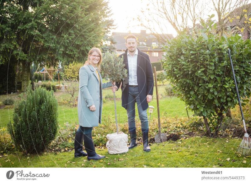 Portrait of smiling couple standing in garden in autumn planting tree portrait portraits gardens domestic garden smile twosomes partnership couples Tree Trees