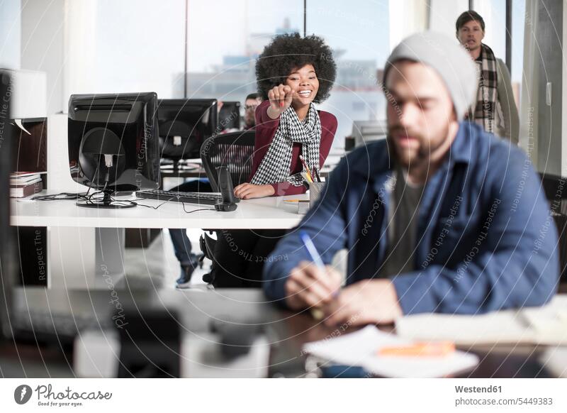 Smiling woman at desk in office pointing at colleague writing down noting offices office room office rooms workplace work place place of work desks business