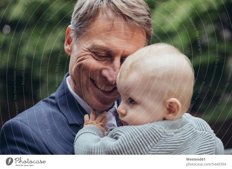 Happy mature businessman holding baby boy outdoors smiling smile father pa fathers daddy dads papa infants nurselings babies Businessman Business man