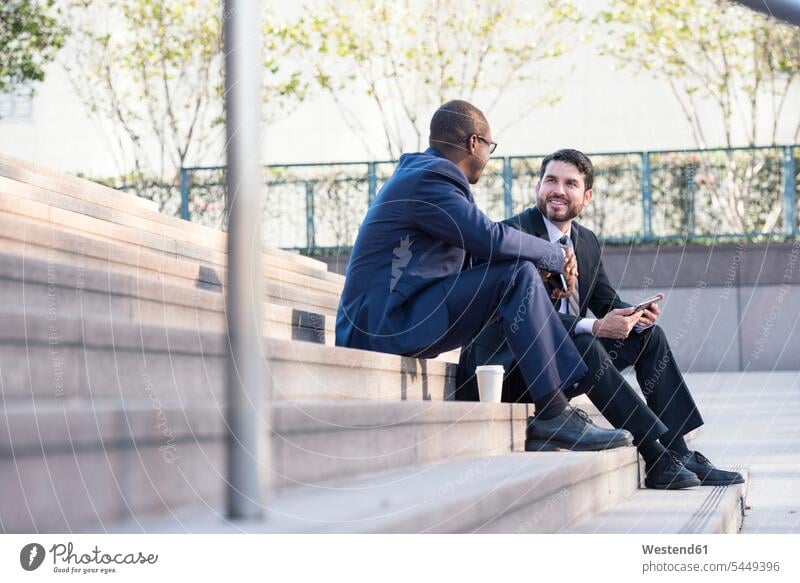 Two businessmen sitting on stairs talking stairway speaking Businessman Business man Businessmen Business men colleagues business people businesspeople