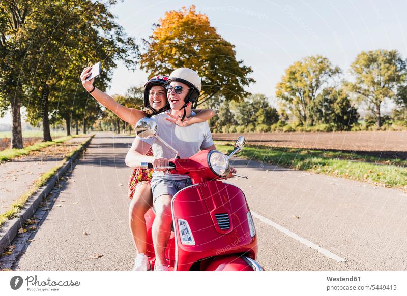 Happy young couple taking a selfie on motor scooter on country road Selfie Selfies happiness happy rural road rural roads country roads twosomes partnership