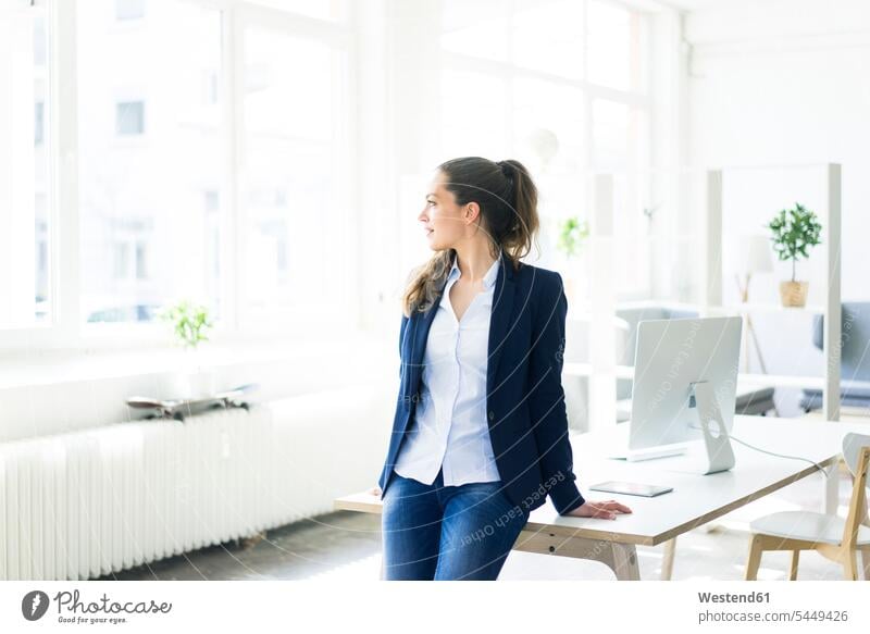 Businesswoman leaning on desk looking out of window businesswoman businesswomen business woman business women females business people businesspeople
