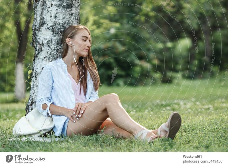 Young woman with earphones relaxing on a meadow park parks ear phone ear phones relaxed relaxation females women earbuds Earbud In-Ear Headphones ear bud