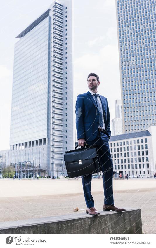 Businessman standing on wall, carrying briefcase on the move on the way on the go on the road brief case Business man Businessmen Business men bag bags