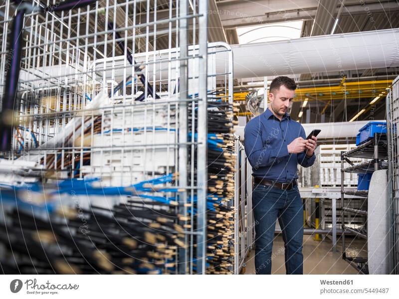 Businessman in factory shop floor looking at cell phone men males Business man Businessmen Business men factories mobile phone mobiles mobile phones Cellphone
