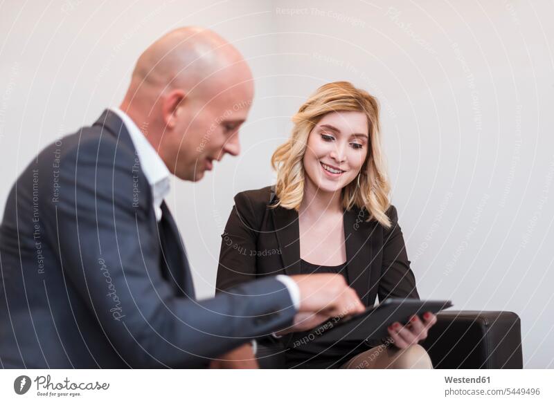 Businessman and businesswoman sitting on couch sharing tablet businesswomen business woman business women smiling smile Business man Businessmen Business men