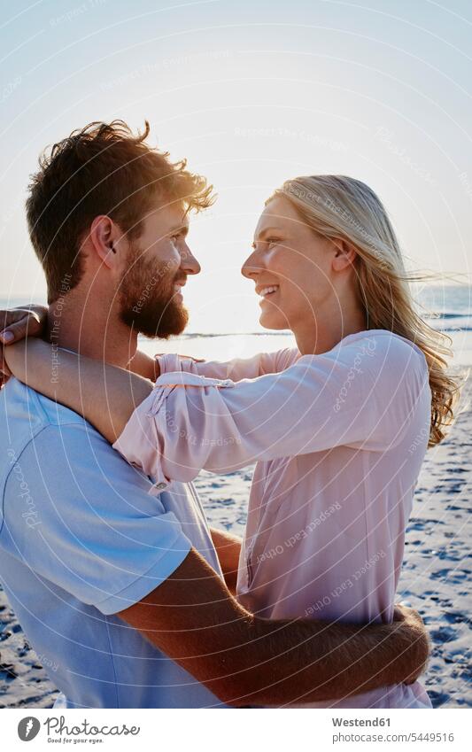 Smiling couple hugging on the beach at sunset smiling smile embracing embrace Embracement beaches happiness happy twosomes partnership couples people persons
