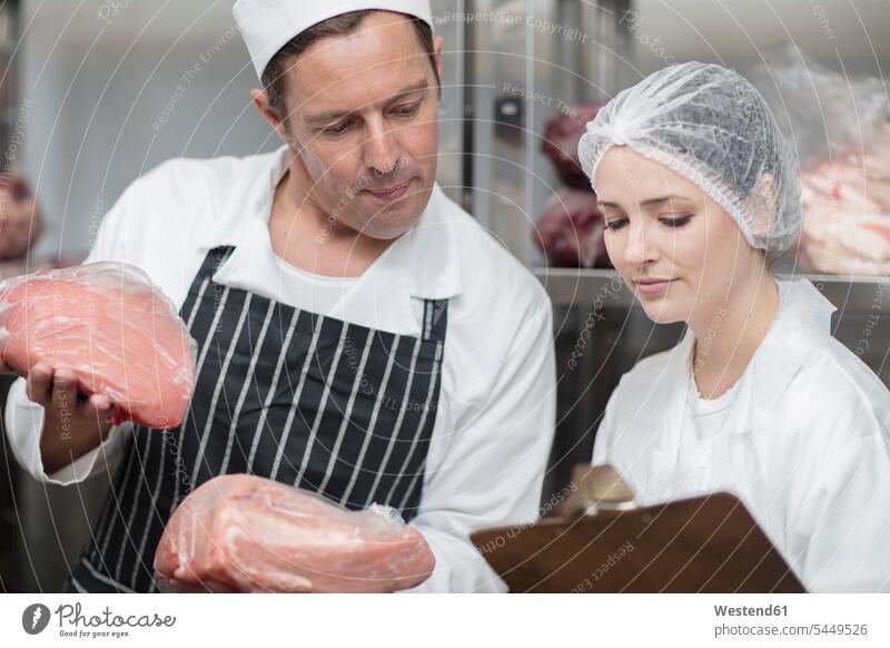 Man and woman with meat and clipboard in storehouse of a butchery working At Work scrutiny scrutinizing charcuterie Food foods food and drink Nutrition