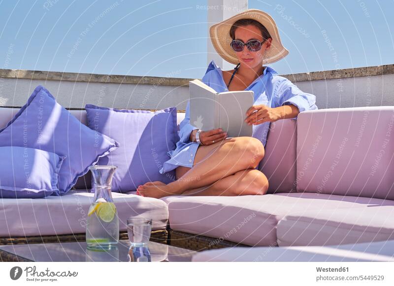 Woman with book relaxing on sun deck Glass Drinking Glasses vacation Holidays Water woman females women reading relaxation books Travel beverages Drinks