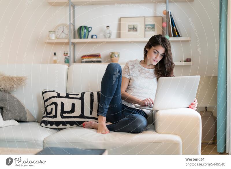 Woman sitting on couch at home using laptop settee sofa sofas couches settees Laptop Computers laptops notebook woman females women computer computers Adults