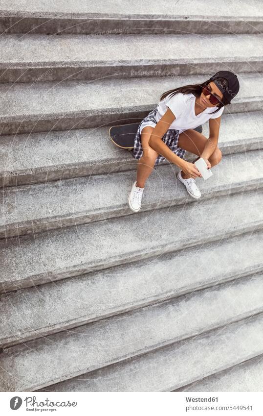 Young woman with skateboard sitting on stairs looking around mobile phone mobiles mobile phones Cellphone cell phone cell phones females women Skate Board