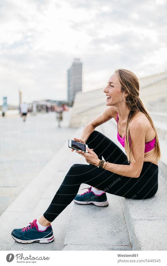 Young woman sitting on stairs after training, using smart phone exercising exercise practising females women laughing Laughter Adults grown-ups grownups adult
