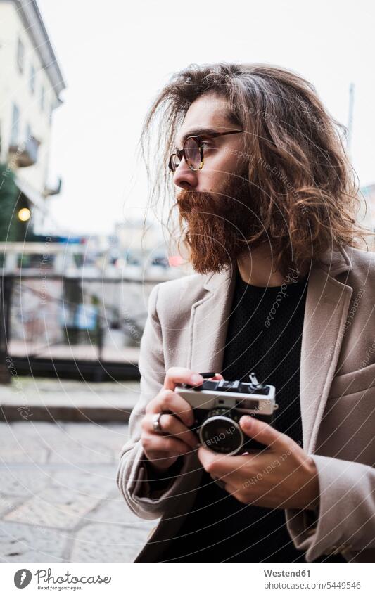 Stylish young man outdoors holding camera looking around men males photographer photographers cameras Adults grown-ups grownups adult people persons human being