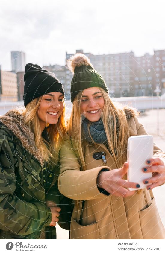 Two friends taking selfie with smartphone mate female friend Selfies photograph smile caps hat hats cell phone cell phones Cellphone mobile mobile phones