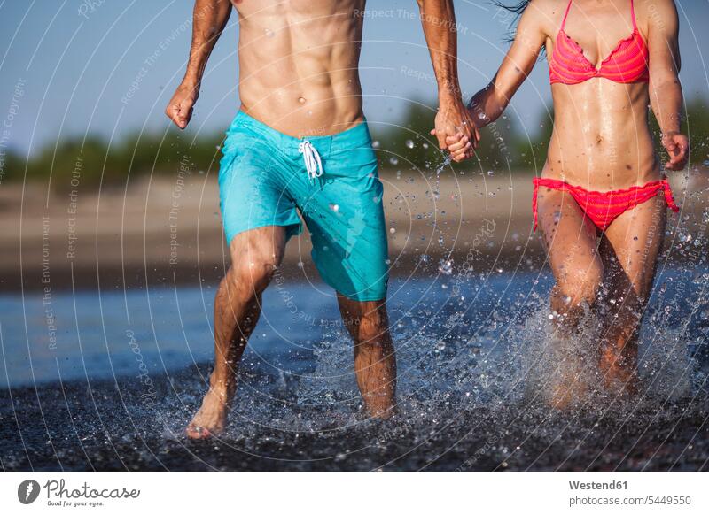 Couple holding hands splashing in water lake lakes Fun having fun funny couple twosomes partnership couples waters body of water people persons human being