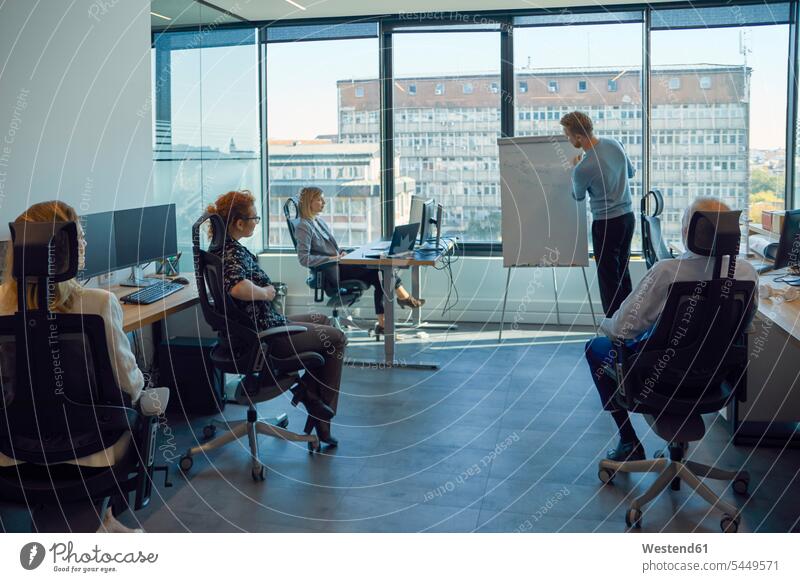 Man leading a presentation at flip chart in office flipchart flip charts flipcharts presentations group of people Group groups of people offices office room
