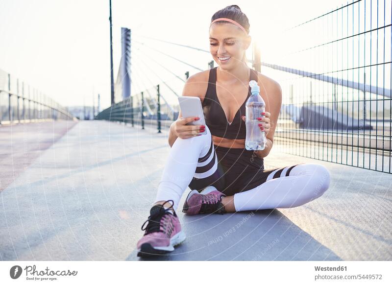 Athletic woman drinking water and checking her phone after workout runner runners mobile phone mobiles mobile phones Cellphone cell phone cell phones resting