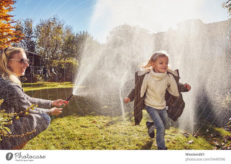 Mother and daughter playing with garden hose in autumn daughters mother mommy mothers ma mummy mama happiness happy child children family families people