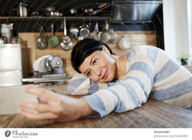 Woman in kitchen resting on table holding cell phone smiling smile Selfie Selfies mobile phone mobiles mobile phones Cellphone cell phones woman females women