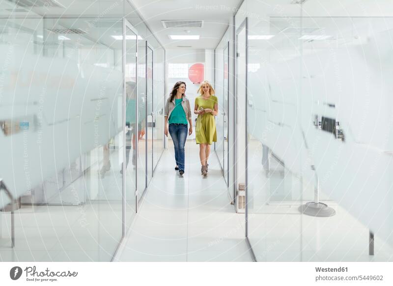 Two female colleagues walking in office corridor offices office room office rooms workplace work place place of work team teamwork teamworking carefree hallway