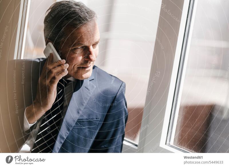 Smiling mature businessman on cell phone looking out of window Smartphone iPhone Smartphones on the phone call telephoning On The Telephone calling Businessman