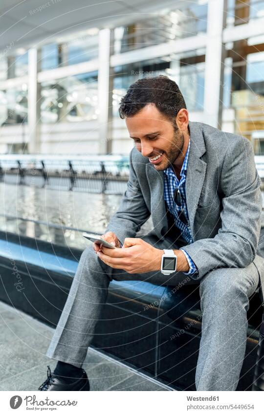 Smiling businessman sending messages with his smartphone in the city smiling smile mobile phone mobiles mobile phones Cellphone cell phone cell phones