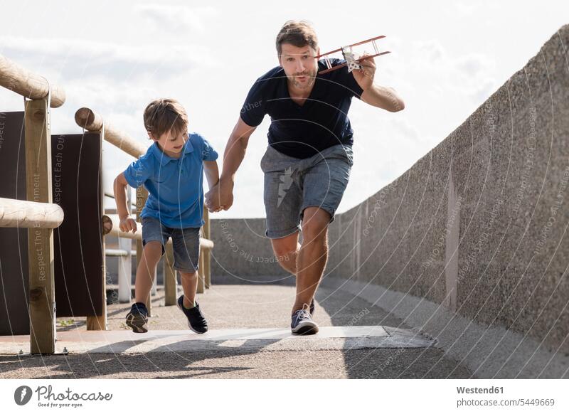 Father and son running with toy plane father pa fathers daddy dads papa happiness happy airplane aeroplanes airplanes playing sons manchild manchildren parents