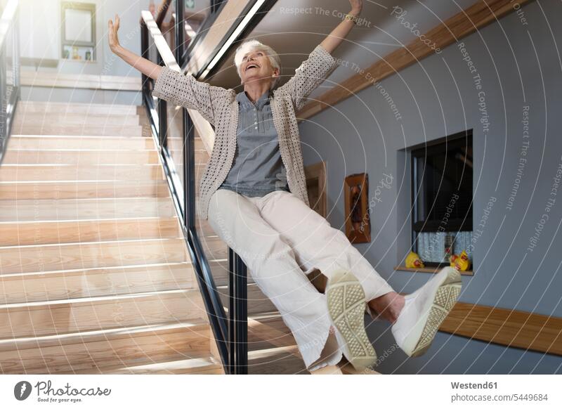 Happy senior woman sliding down a staircase senior women elder women elder woman old Railing Railings slide retirement home nursing home stairs stairway