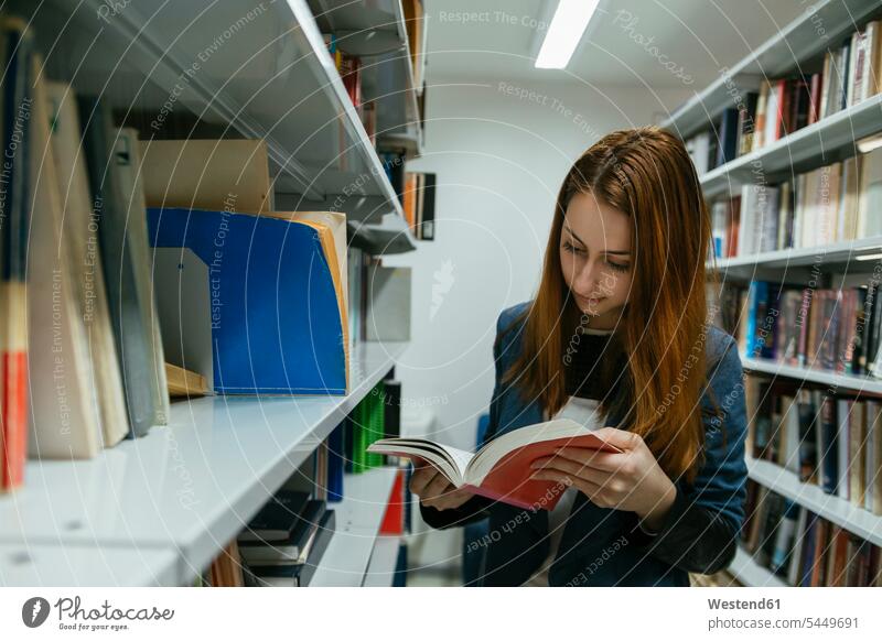 Female student reading book in a library learning female students books higher education building buildings built structure built structures bookshelf