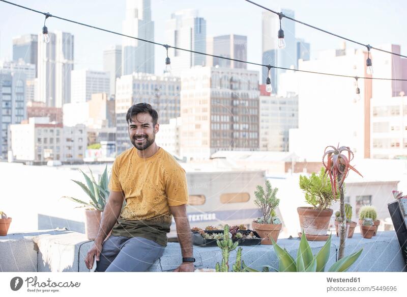 Young man sitting on rooftop terrace men males roof terrace deck carefree Seated Adults grown-ups grownups adult people persons human being humans human beings