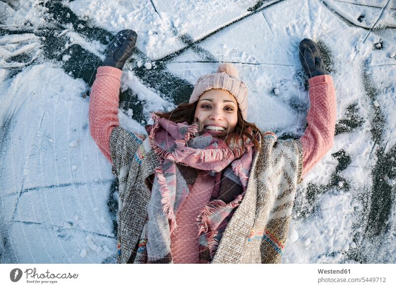 Portrait of happy woman lying down on frozen lake surface woolly hat Wooly Hat Knit-Hat Knit Hats wool cap laying down lie smiling smile females women hats caps