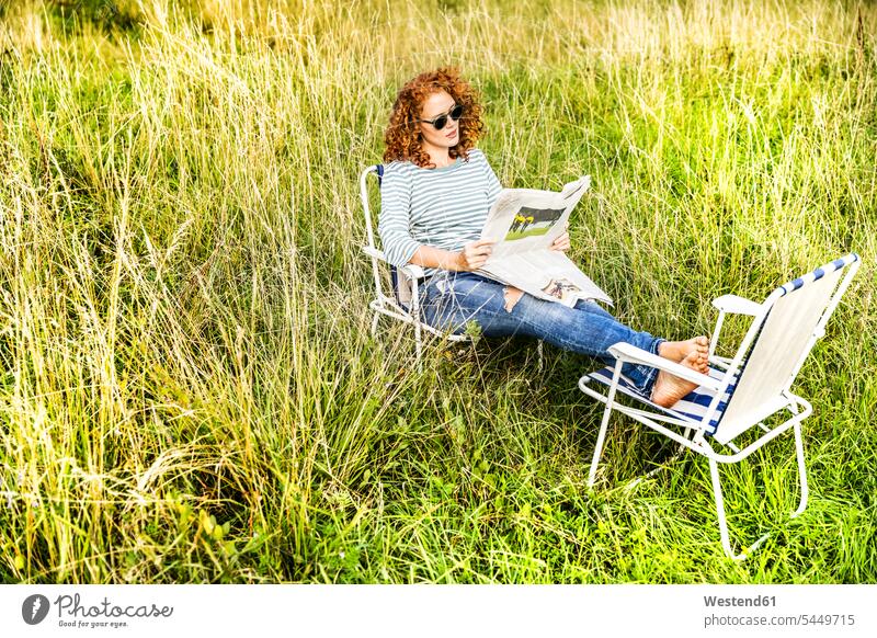 Young woman relaxing on a meadow reading newspaper newspapers females women Adults grown-ups grownups adult people persons human being humans human beings