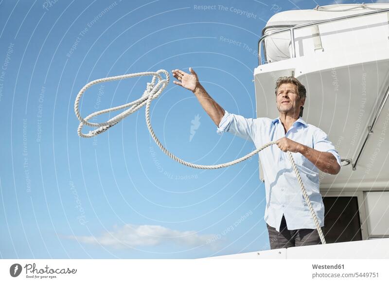 Mature man on motor yacht throwing rope men males motor yachts Adults grown-ups grownups adult people persons human being humans human beings Yacht Yachts ship