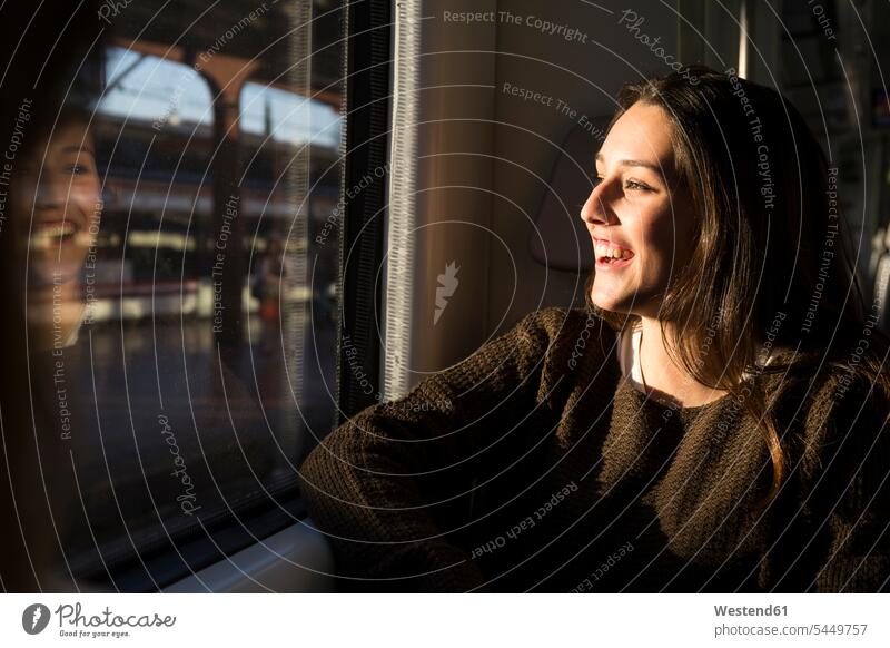 Happy young woman on a train looking out of window females women railway railroad transportation Adults grown-ups grownups adult people persons human being