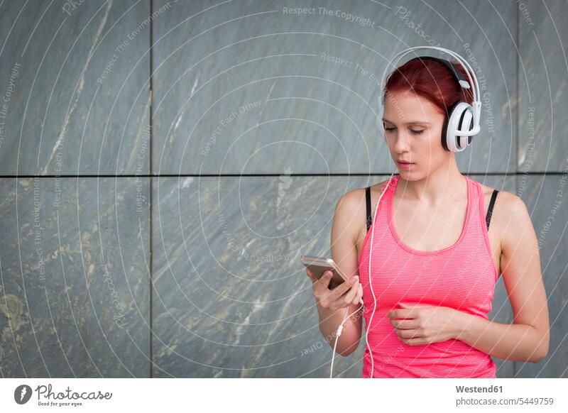 Woman in sports outfit wearing headphones, listening music woman females women workout working out work out Smartphone iPhone Smartphones exercising exercise