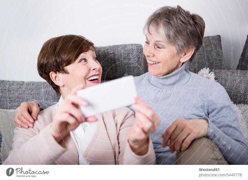 Two senior women sitting on couch, female friends together Selfie Selfies elder women elder woman old senior woman Seated photographing mobile phone mobiles