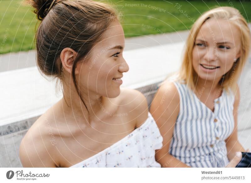 Two smiling young women talking outdoors female friends smile speaking woman females happiness happy mate friendship Adults grown-ups grownups adult people
