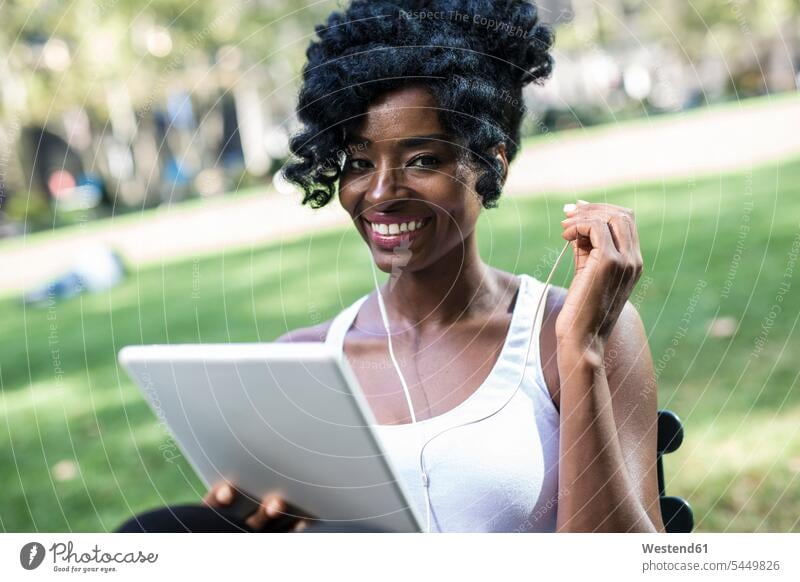 Portrait of smiling woman sitting in a park using tablet and earphones portrait portraits females women Adults grown-ups grownups adult people persons