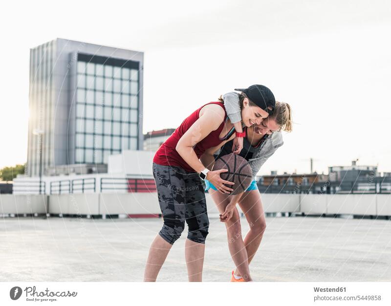 Two happy women with basketball on parking level in the city basketballs embracing embrace Embracement hug hugging smiling smile woman females female friends
