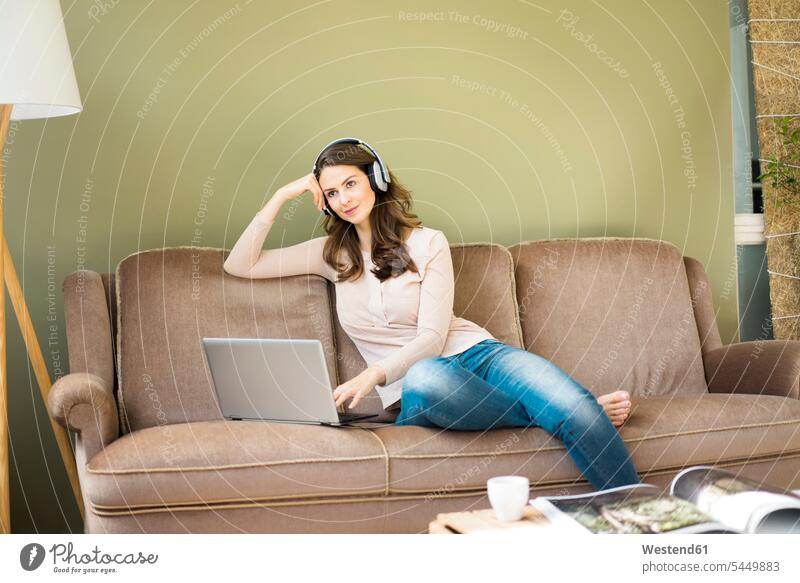 Young woman with headphones sitting on couch using laptop Laptop Computers laptops notebook settee sofa sofas couches settees headset females women computer