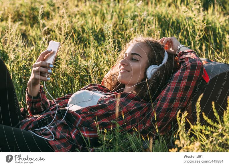 Teenage girl with backpack lying on a meadow listening music with headphones and cell phone Teenage Girls female teenagers headset Teenager Teens people persons