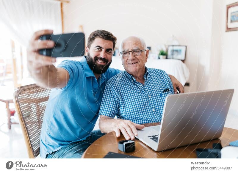 Portrait of adult grandson and his grandfather taking selfie with smartphone at home grandsons portrait portraits grandpas granddads grandfathers Selfie Selfies
