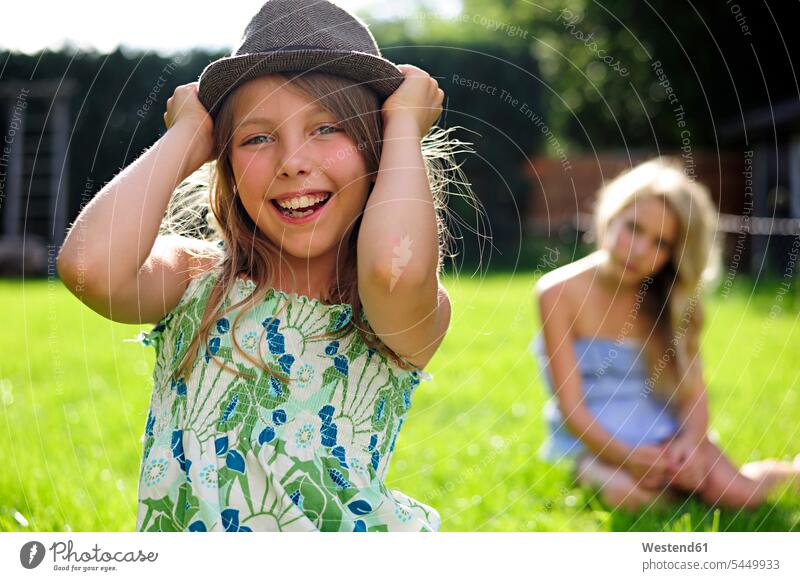 Happy playful girl putting on a hat in garden Fun having fun funny laughing Laughter gardens domestic garden females girls hats positive Emotion Feeling